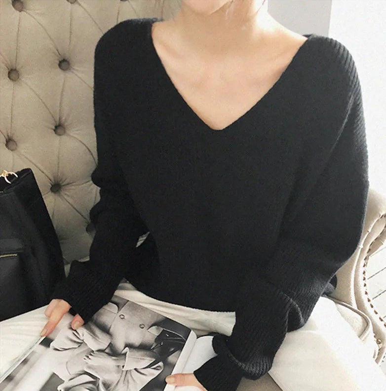 Person wearing a black sweater sitting on a couch with a magazine. #Color_Black