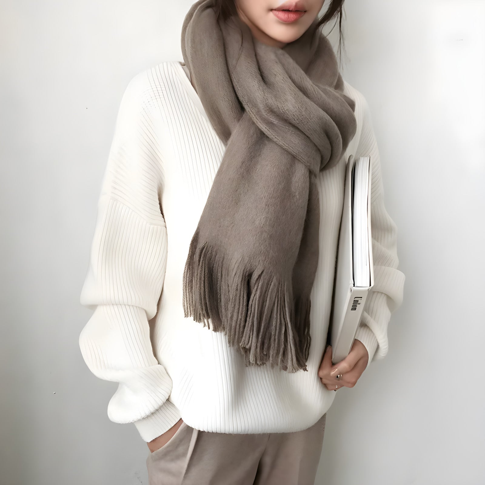 Person wearing a white sweater and brown scarf holding a book against a plain background #Color_White