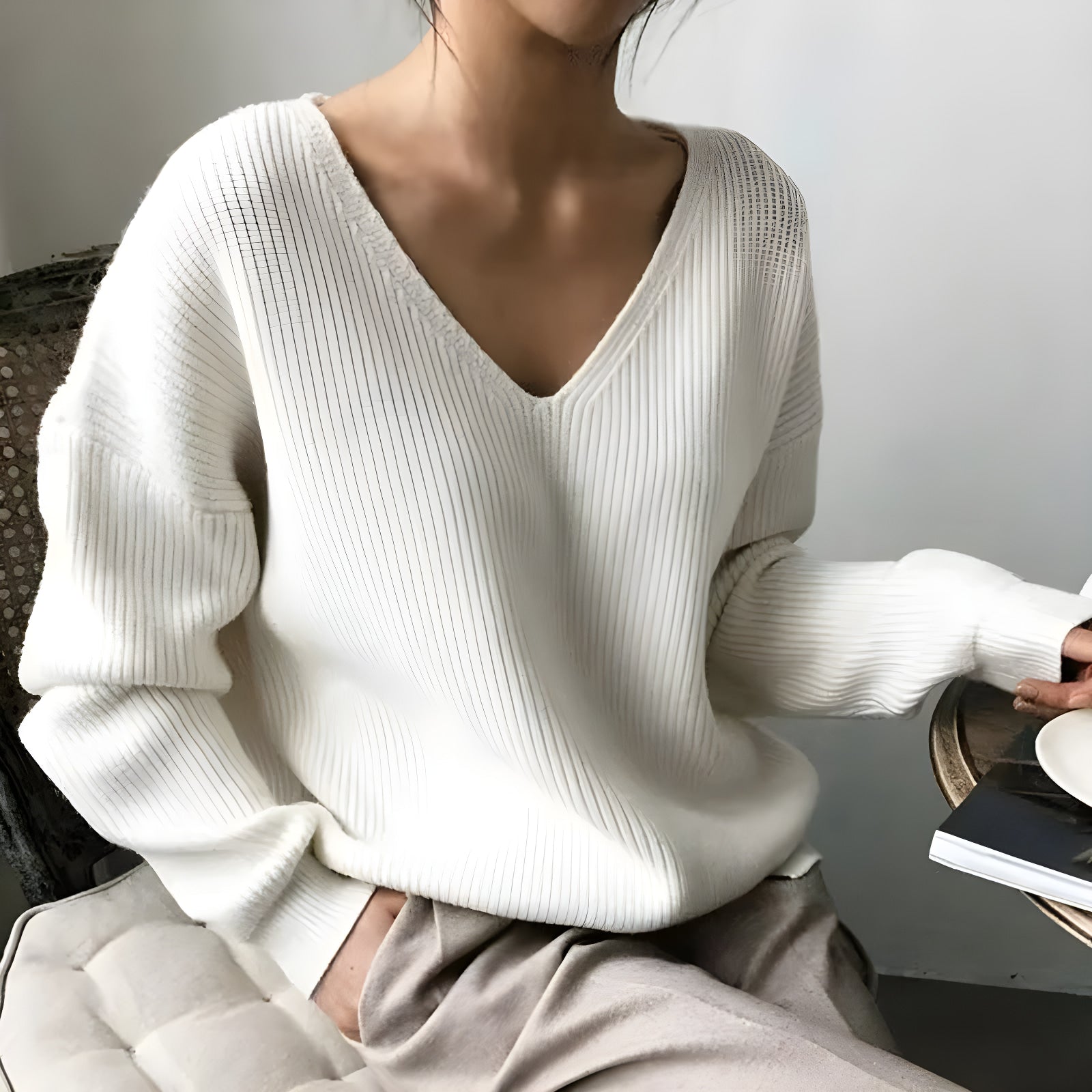 Person wearing a white sweater sitting on a chair with a neutral background  #Color_White